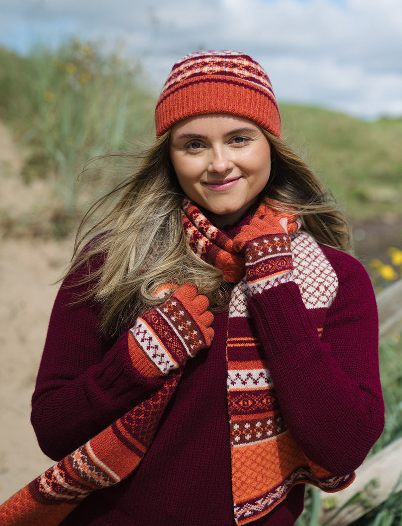 Girl wearing orange fair isle fingerless gloves, hat and scarf with burgundy jumper